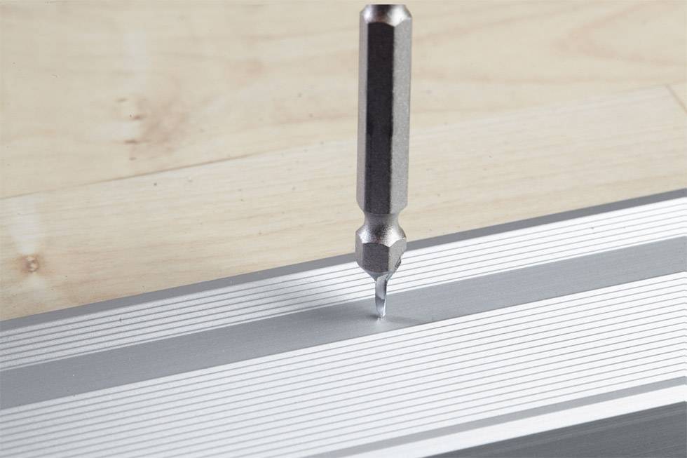 Close-up of a metal tool punching a precise indentation into a ruler on a wooden surface.