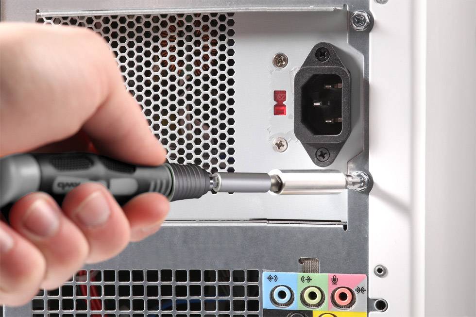 A hand is using a screwdriver to remove the casing of a computer tower. The visible rear side reveals connections and power supply.