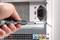 A hand is using a screwdriver to remove the casing of a computer tower. The visible rear side reveals connections and power supply.