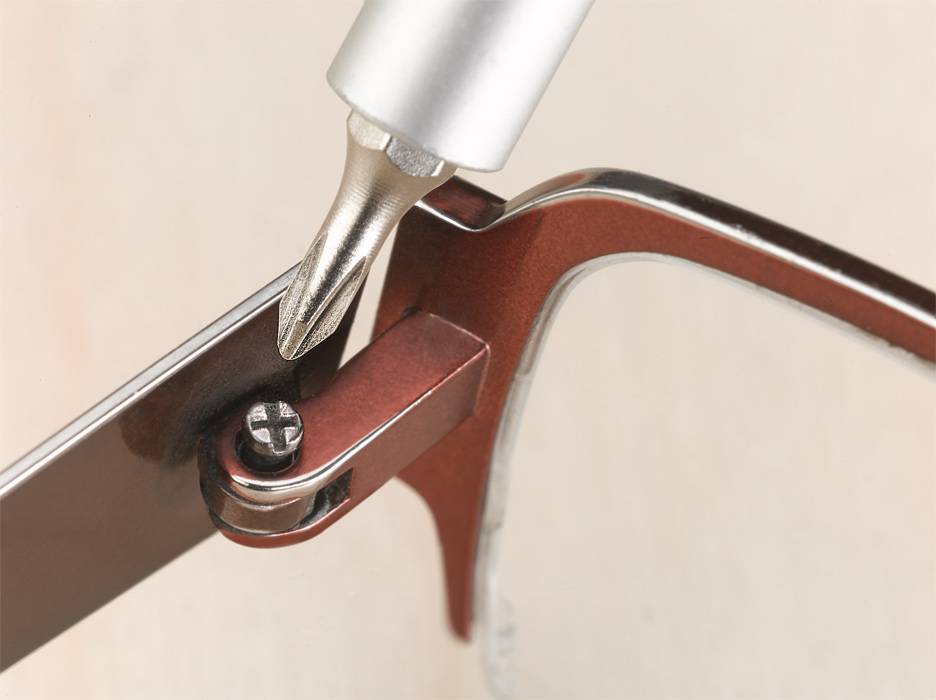 A screwdriver tip tightens a small screw on the spectacle frame. Close-up of the glasses frame and tool use.