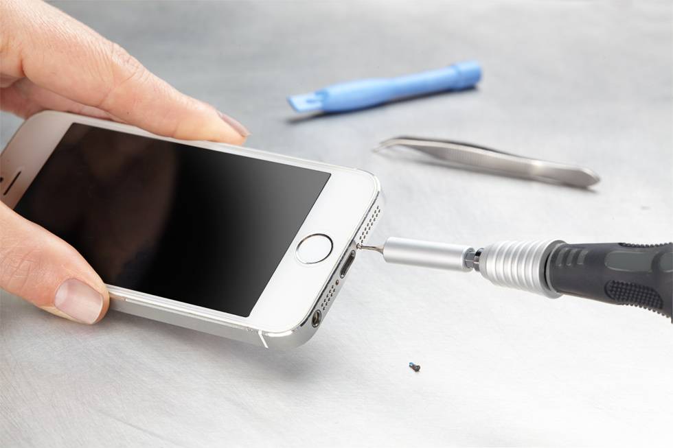 A person is repairing a smartphone with a screwdriver; tools in the background.