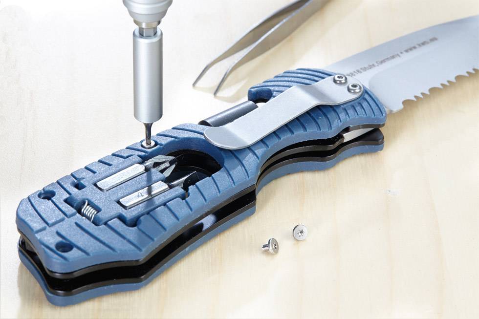 A blue penknife handle is being secured with a screwdriver. Part of the blade is visible. Two screws are lying beside it.