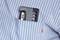A black pen is sitting in the breast pocket of a blue and white striped shirt.