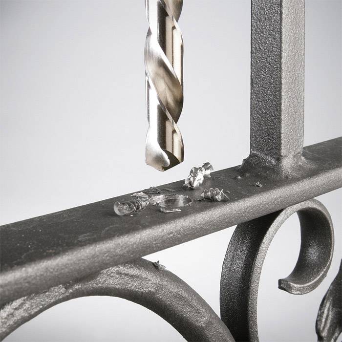 A drill penetrates a metal fence, metal shavings lie on the surface.