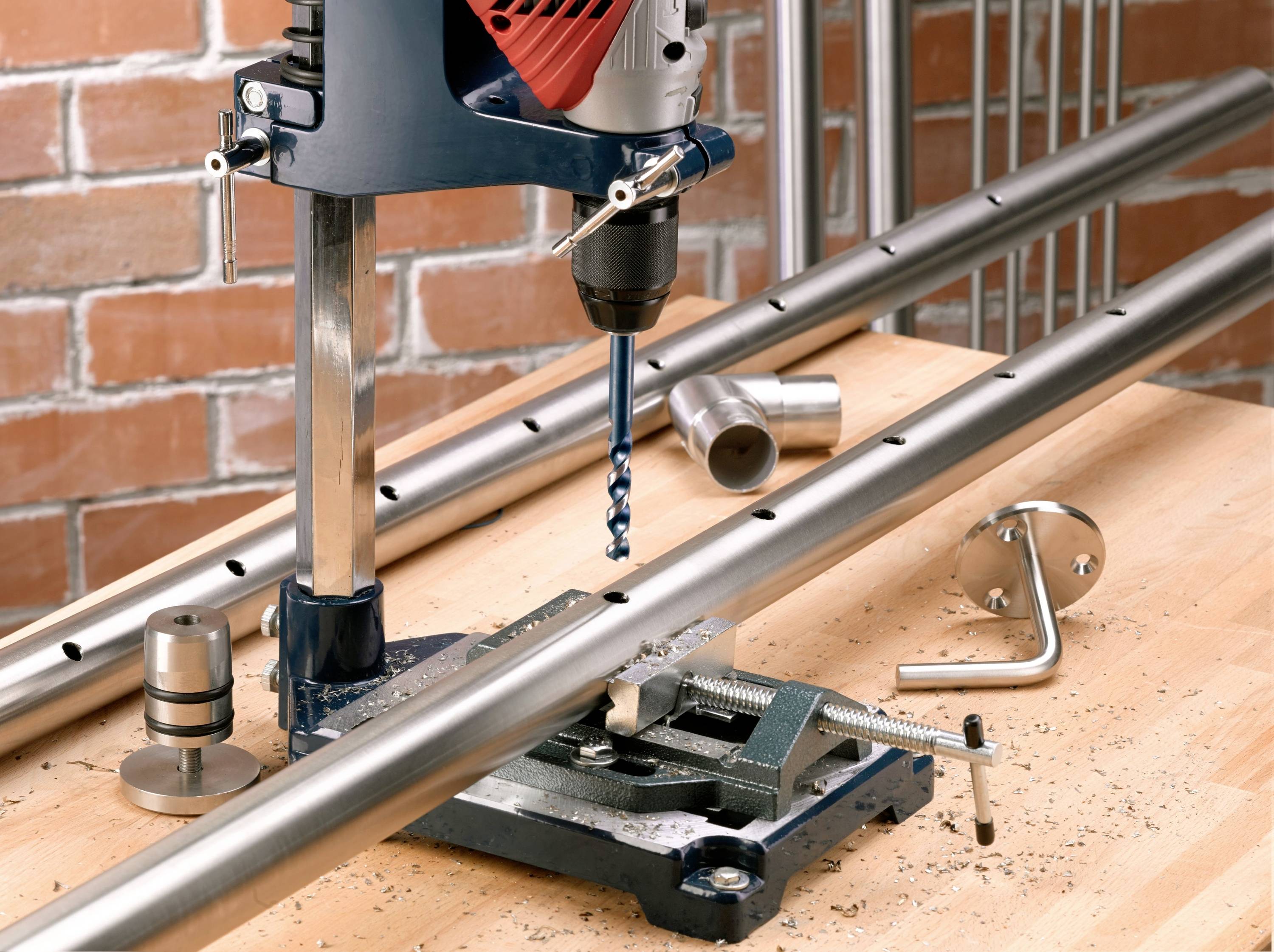 A drill machine is machining metal pipes that are secured on a workbench. Metal shavings are scattered around the device.