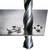 A drill is boring through a metal sheet, surrounded by metal shavings. The drill has nearly completely penetrated and shavings are lying around the hole.