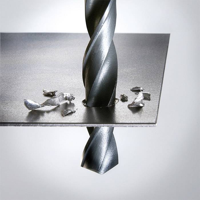 A metal drill penetrates a metal sheet, with metal shavings scattered around the hole.