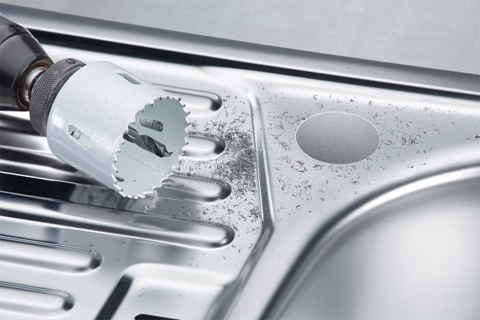 Drill bit creates hole in metal sink; metal shavings visible.