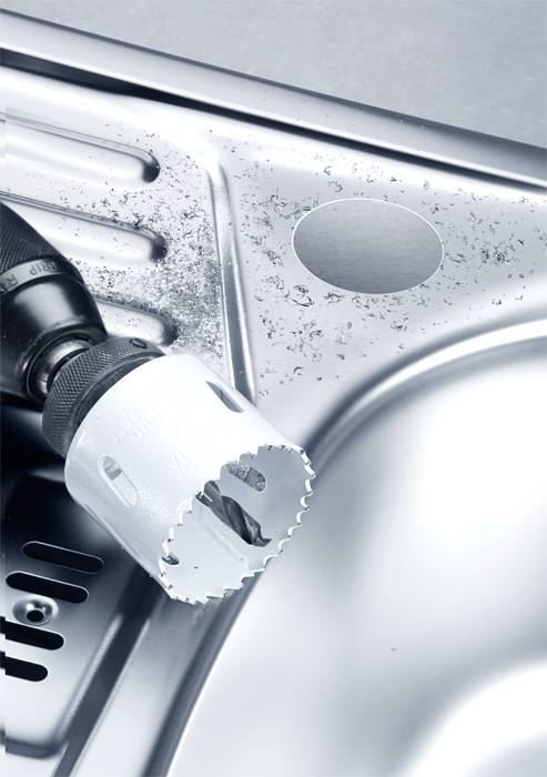 A built-in refrigerator installation using a drill and an attachment cutting a hole in a stainless steel sink.