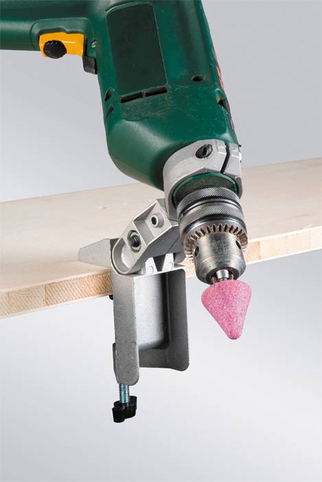Drill with grinding attachment grinds the edge of a wooden board. The device is attached to a metal holder.