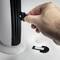 A hand opens the battery compartment of an electrical device. Beside it, a battery cover and batteries are lying on a surface.