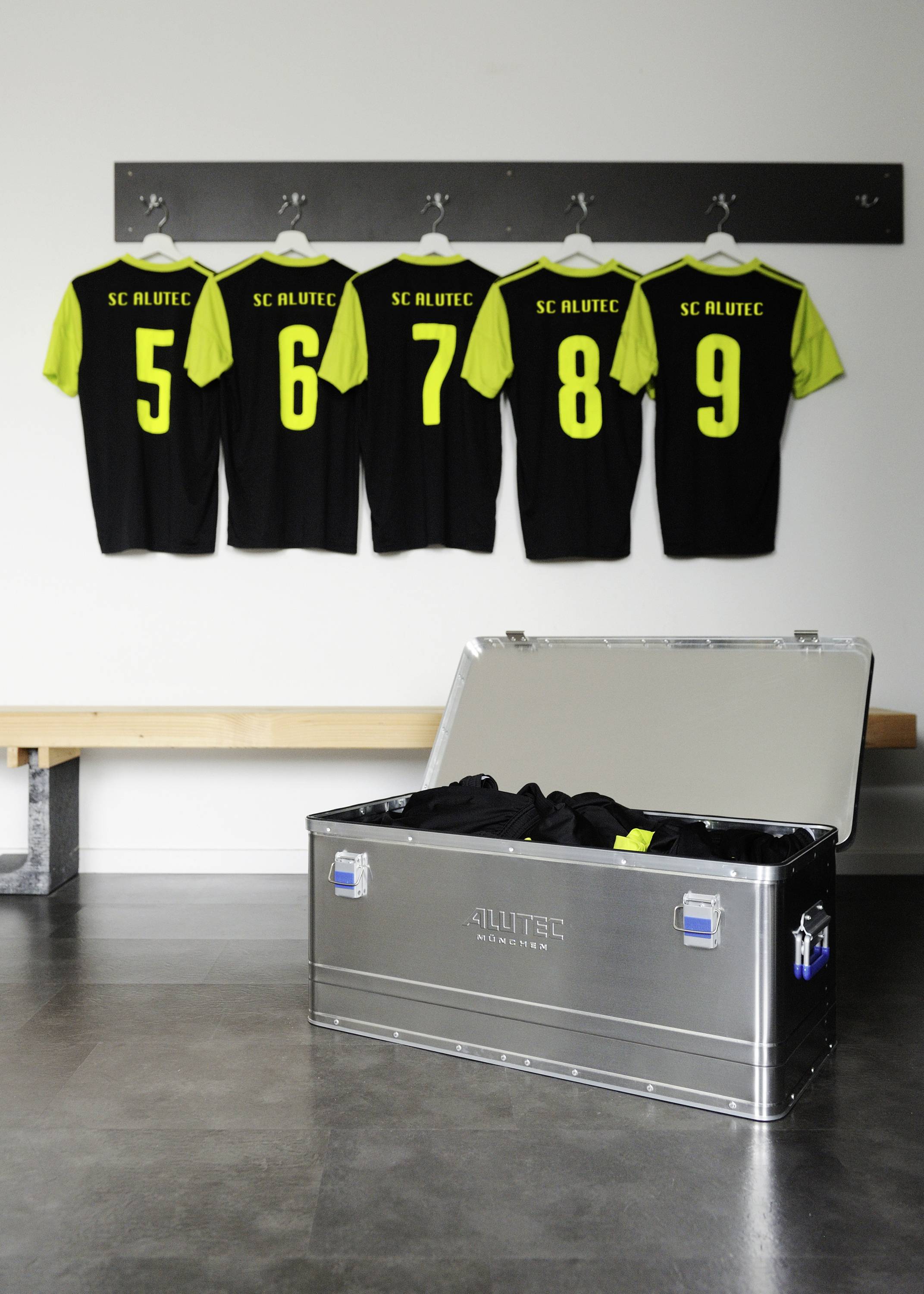 Five black sports jerseys with yellow numbers (5-9) are hanging on the wall, next to an opened metal box containing additional jerseys.