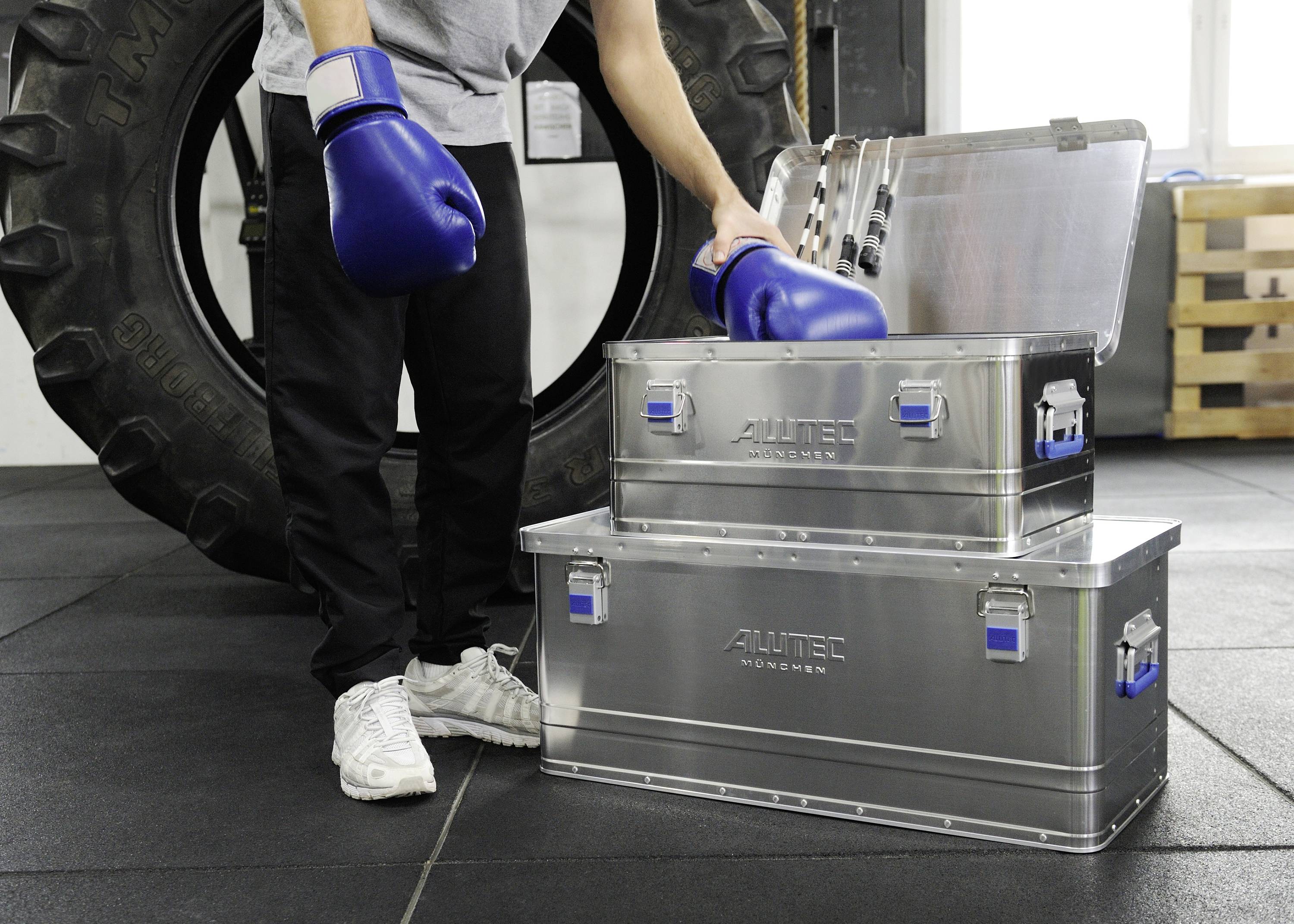 'A person wearing blue boxing gloves pulls something out of metal boxes in the gym.'