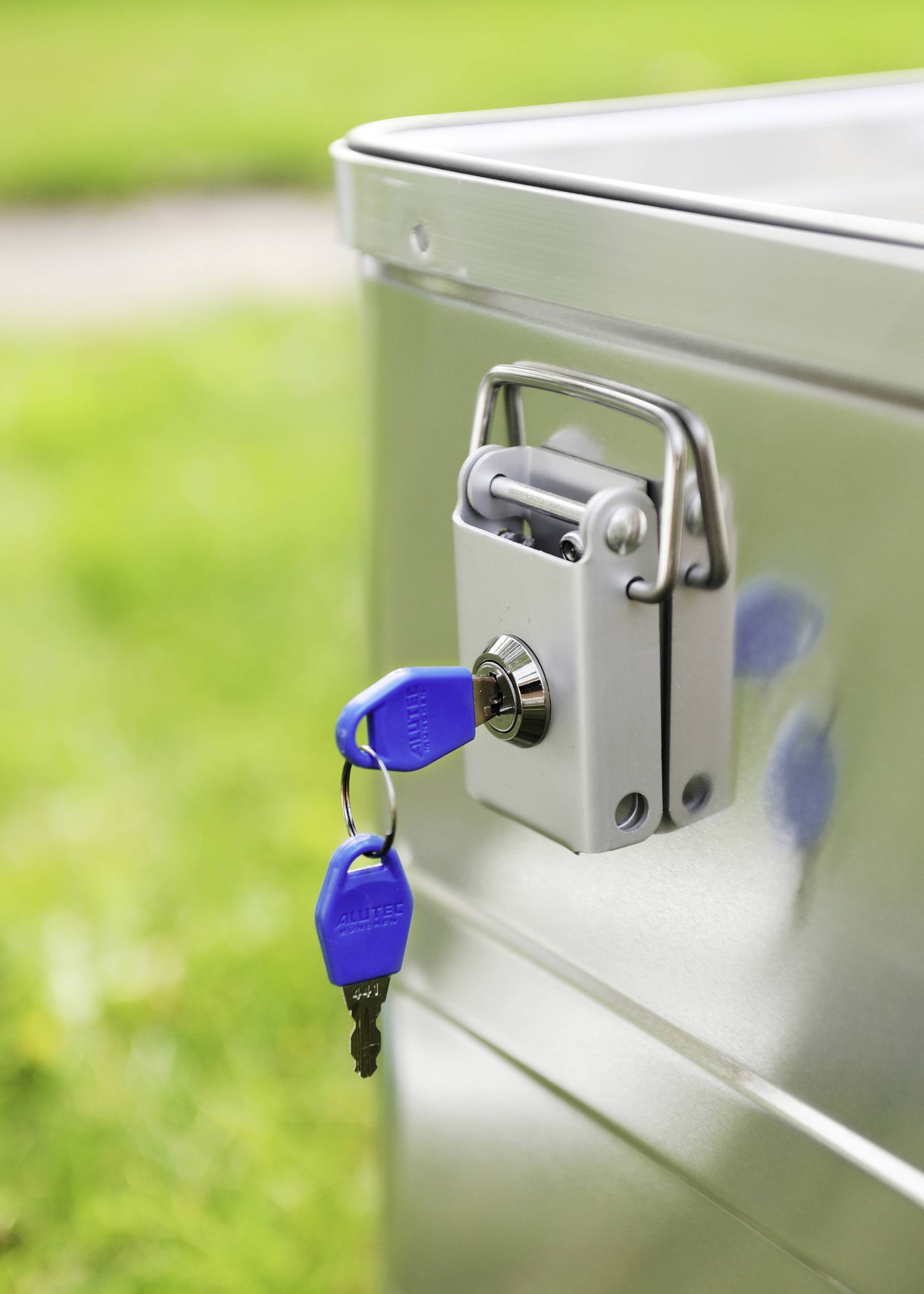 Silver metal box with a blue key in the lock against a green background. The locksmith service demonstrates locking options.