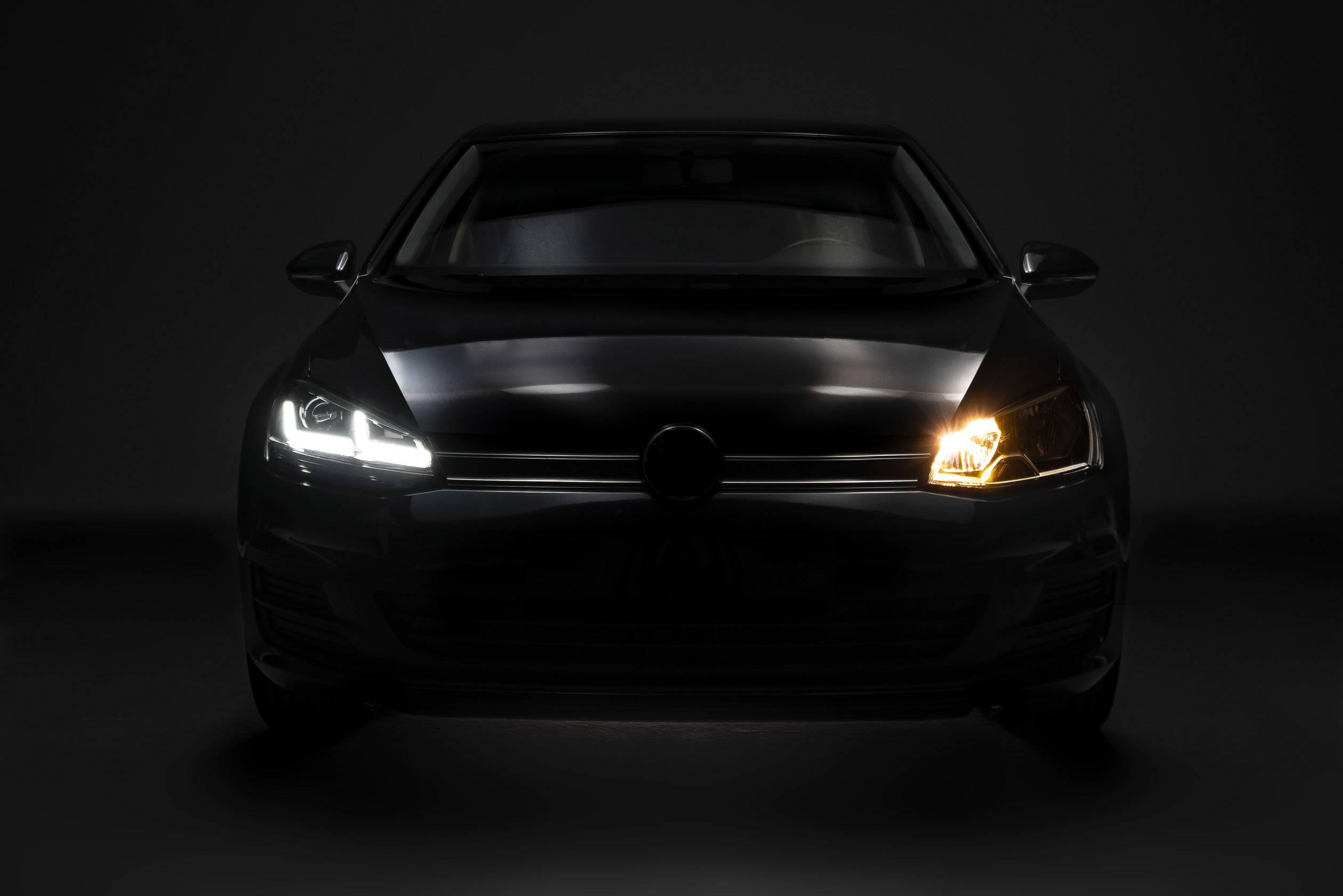 A car in a dark environment with the headlight switched on on the left side and switched off on the right side.