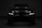 A black car is parked in a dark room. Its headlights are switched on and shine brightly, emphasised by the darkness.