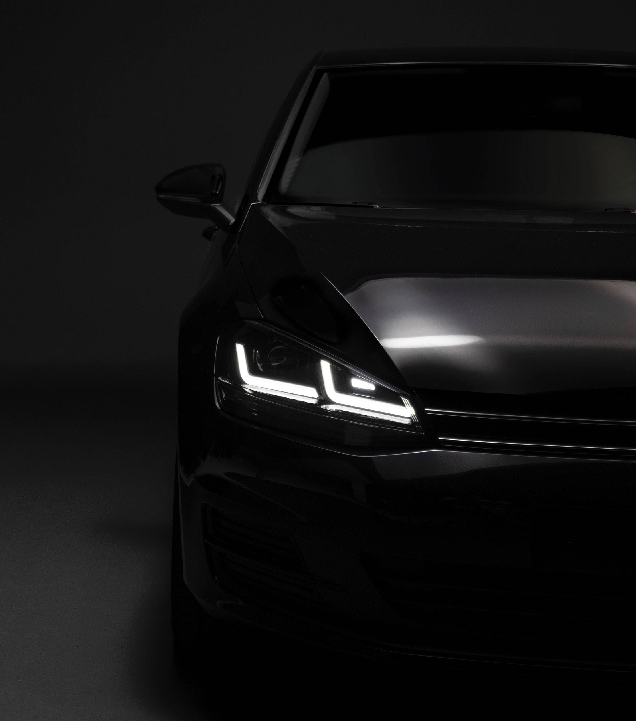 Dark car with headlights on against a black background. Vehicle visible from the front right, light emphasised.