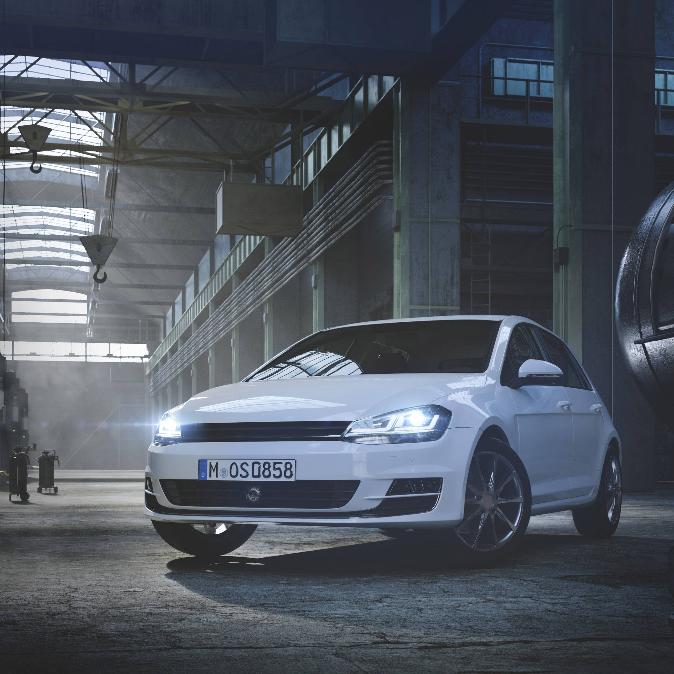 A white car is parked in an illuminated warehouse. It is visible from the front right. Windows and ceiling have metal structures.