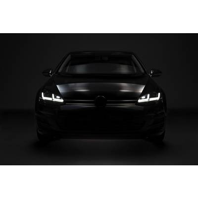 A black car viewed from the front with headlights switched on, standing in a dark room. The focus is on the distinctive light design.