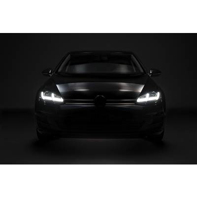 A black car with headlights switched on is positioned head-on in a dark environment.