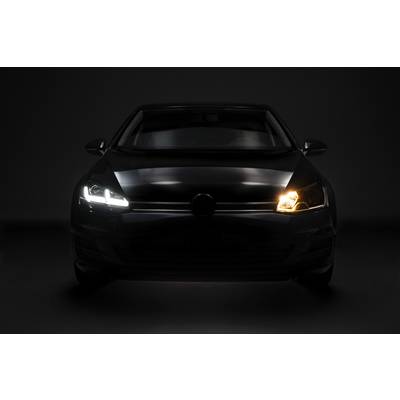 A car with a headlight switched on on the right side and a headlight switched off on the left side, against a dark background.