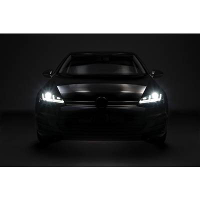 A car at night, photographed head-on, with dipped headlights illuminating the dark surroundings.