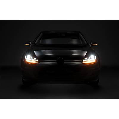 A car with headlights and indicator lights switched on is visible from the front in the darkness.
