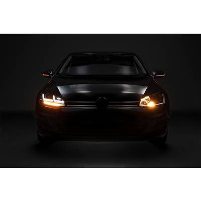 A car in a dark room, its lights switched on and glowing in orange and white, with the headlights activated.