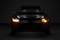 A car in a dark room, its lights switched on and glowing in orange and white, with the headlights activated.