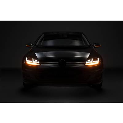 A black car with headlights switched on and flashing yellow lights, viewed head-on in a dark environment.