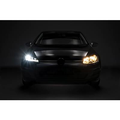 A car with its dipped and full beam headlights switched on is positioned facing forward in a dark room.