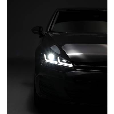 A black car with headlights switched on in a dark room. Only the front section of the vehicle is visible.