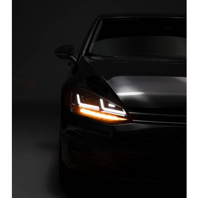 A dark car with headlights switched on in a dimly lit space, showcasing the vehicle's modern styling.