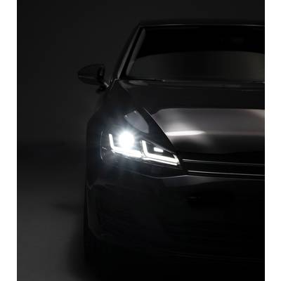 A dark car with headlights on in a dark environment, showcasing modern vehicle design.