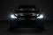Car with dipped headlights on, viewed from the front, in a dark environment.