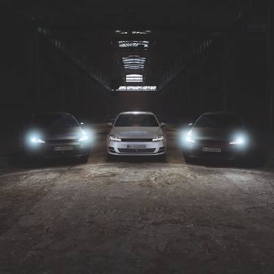 Three cars with headlights switched on stand in a dark, empty hall, symbolising modernity and technology.