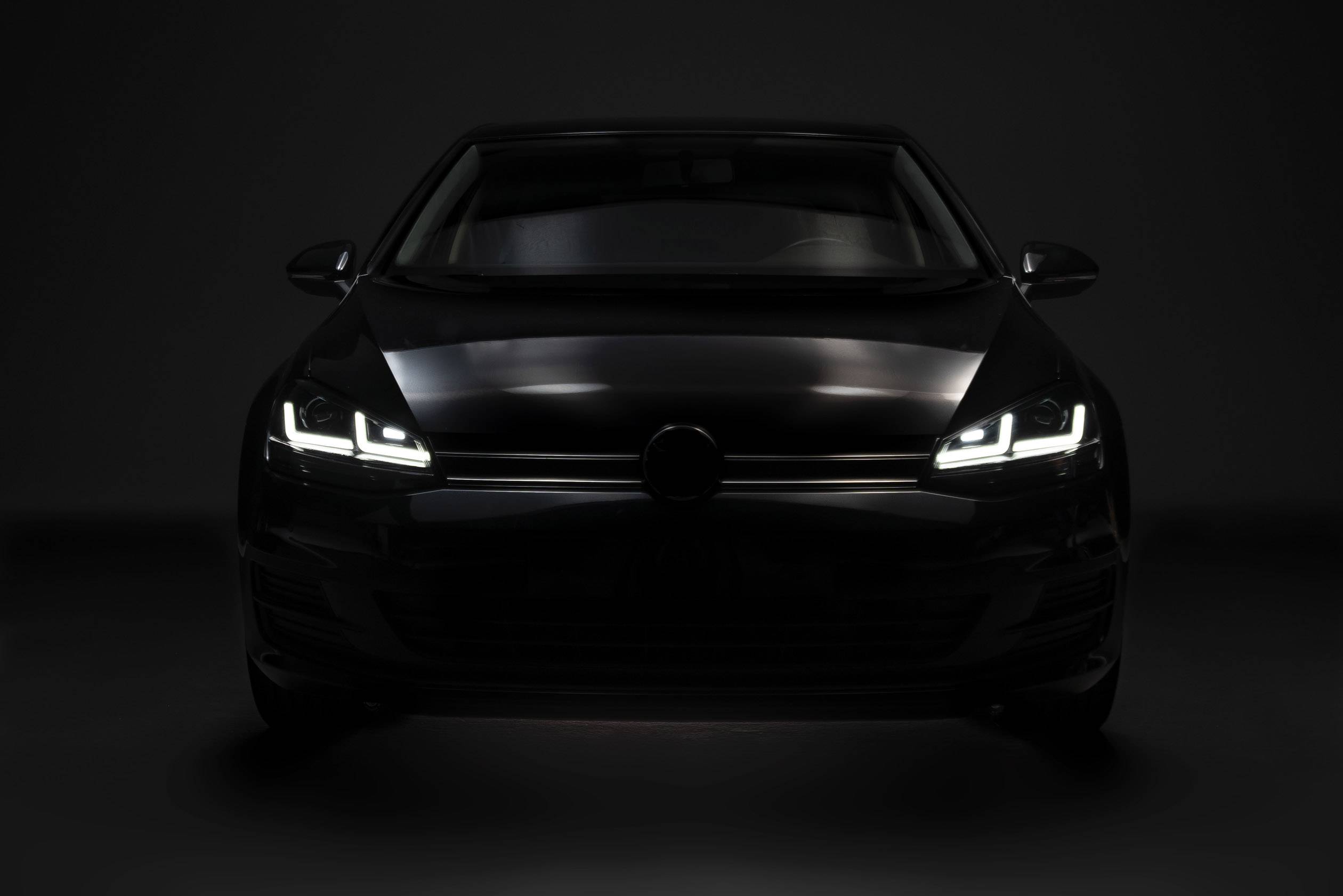 A car in a dark environment from the front, with headlights switched on, casting bright light beams.