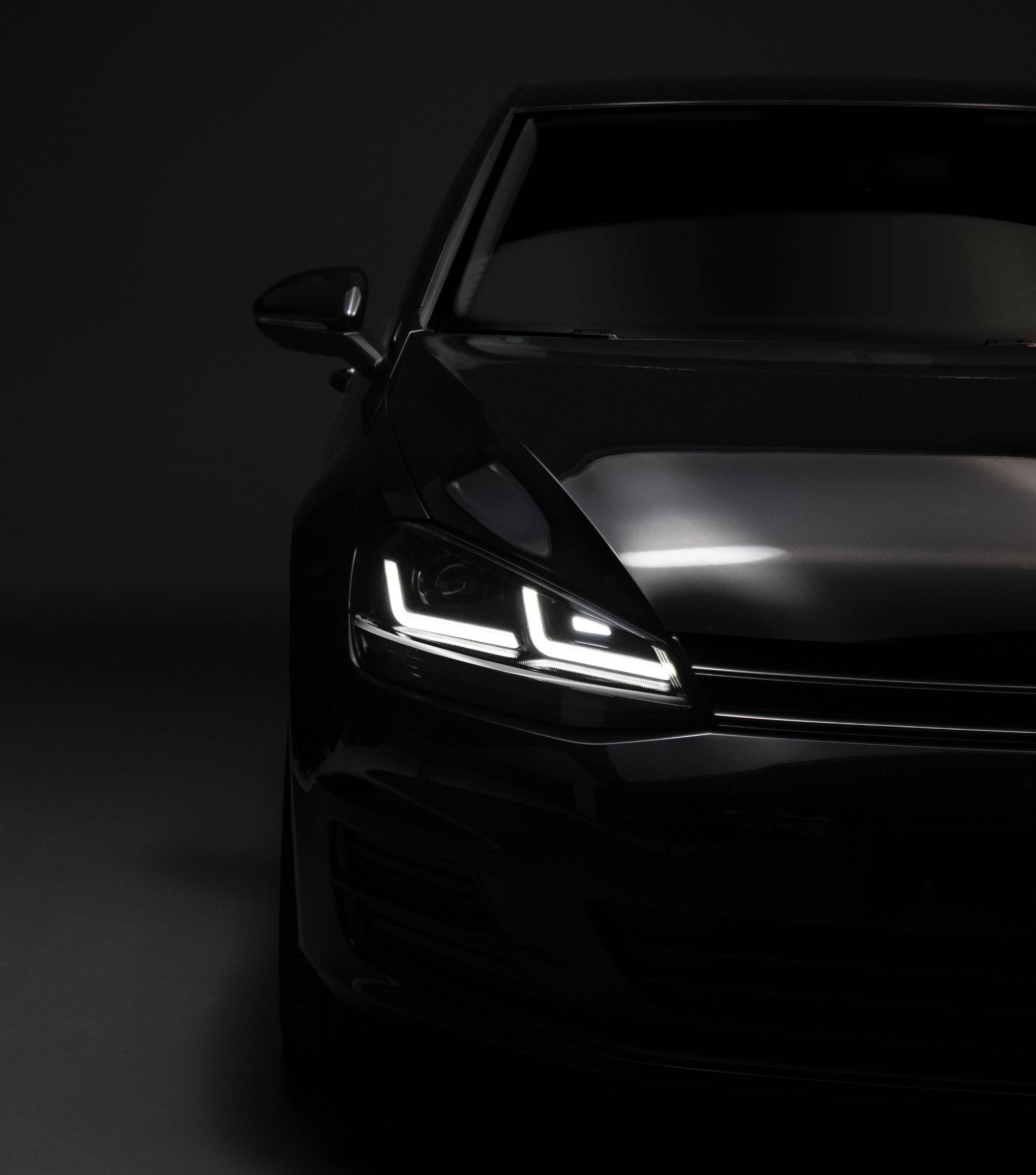 Half-close-up of a black car against a dark background, headlights switched on and glowing, modern vehicle aesthetics.