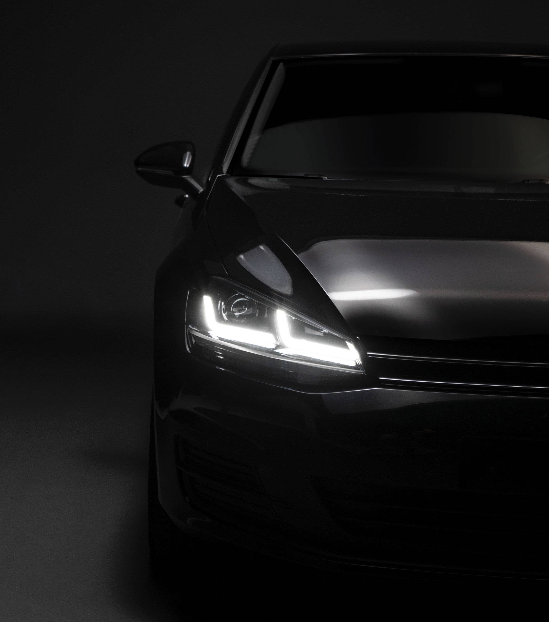 A car with its headlights on in a dark environment, visible on the right side of the image.