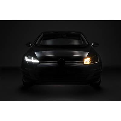 A car is parked in a dark environment, with a functioning headlight on the right side and a faulty one on the left.