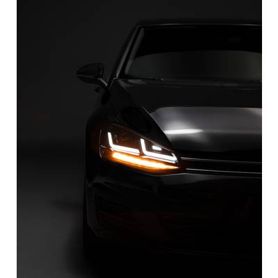 Front view of a black car in the shadow with illuminated LED headlights, positioned on the right side of the image. Dark background.