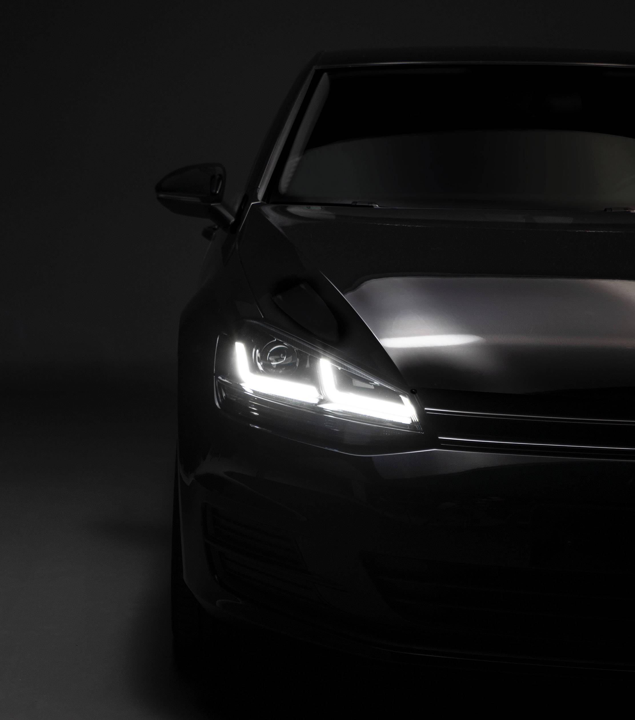 Partial view of a black car in dim light, showing illuminated headlights and emphasising the modern vehicle design.