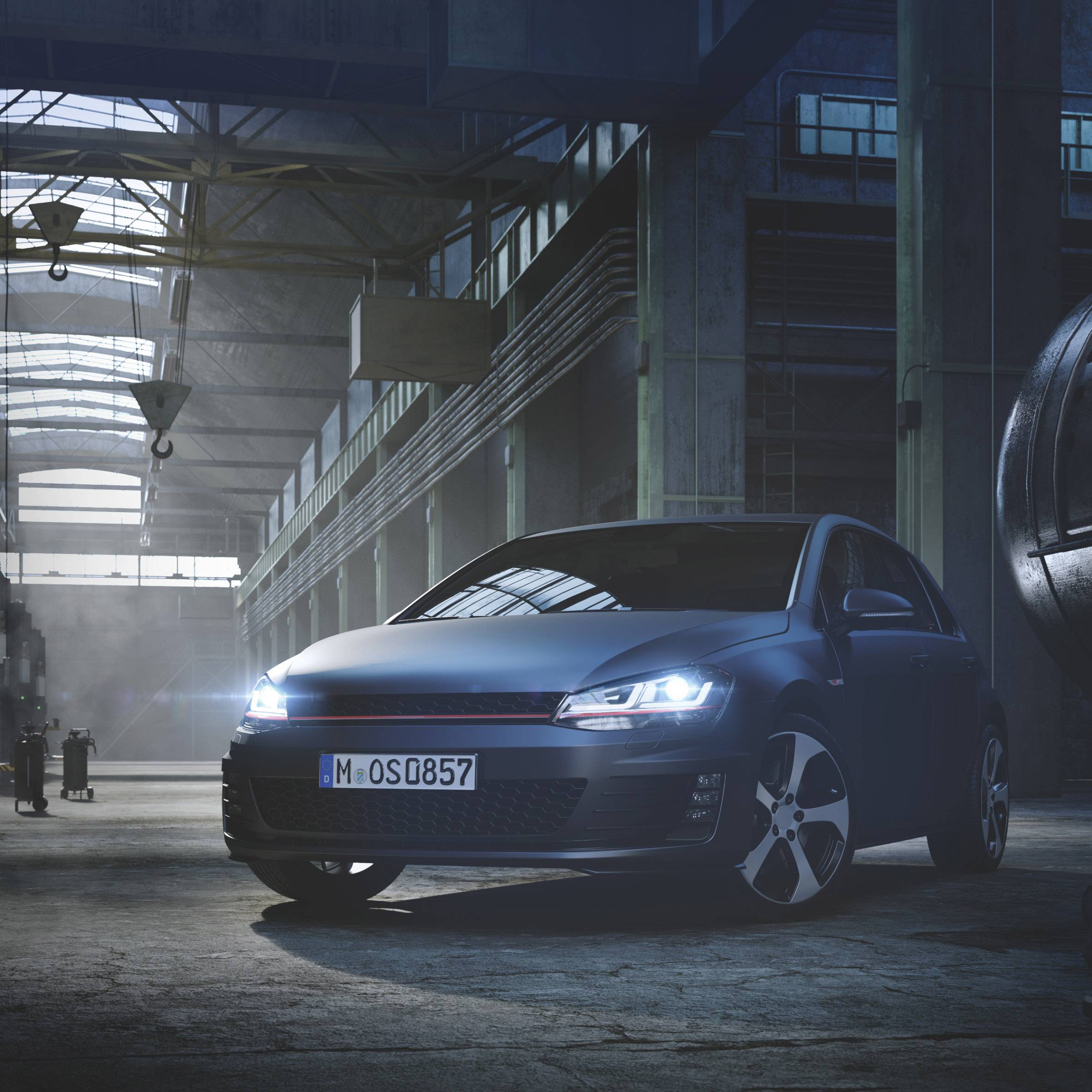 A car is standing in an industrial hall with high ceilings and large windows. It is illuminated by the headlight.