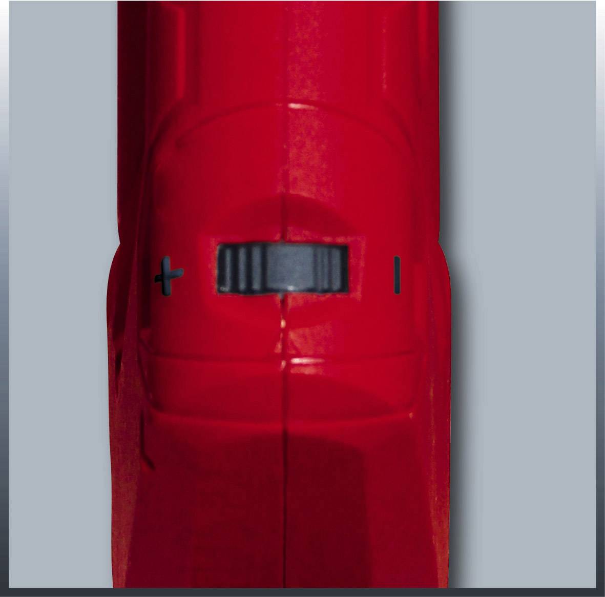 Close-up of a red switch with a black rotary knob positioned between plus and minus signs.