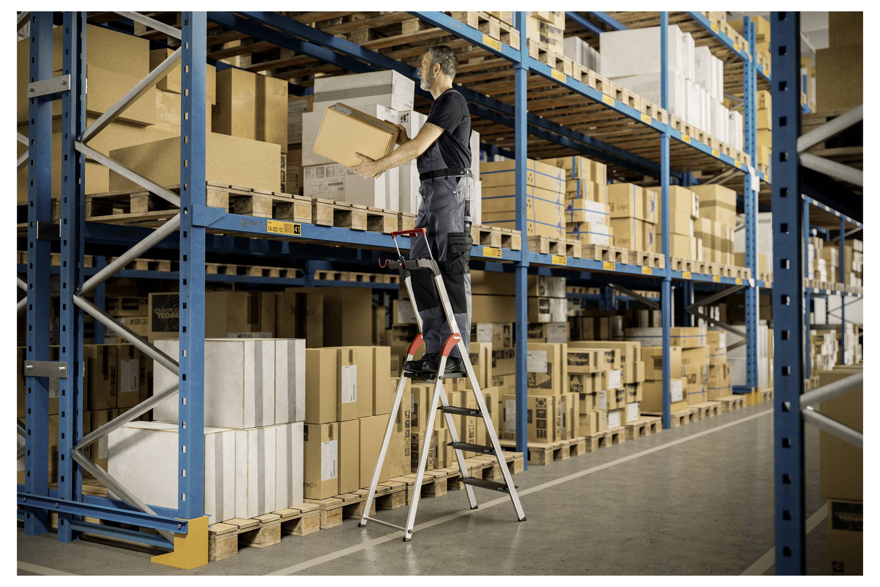 A warehouse worker stands on a ladder to organize boxes on a high shelf, surrounded by rows of stacked packages and shelves.