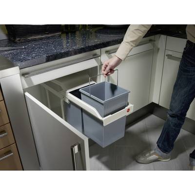 A person opens a cupboard beneath the sink and lifts a removable bin from a waste separation system.