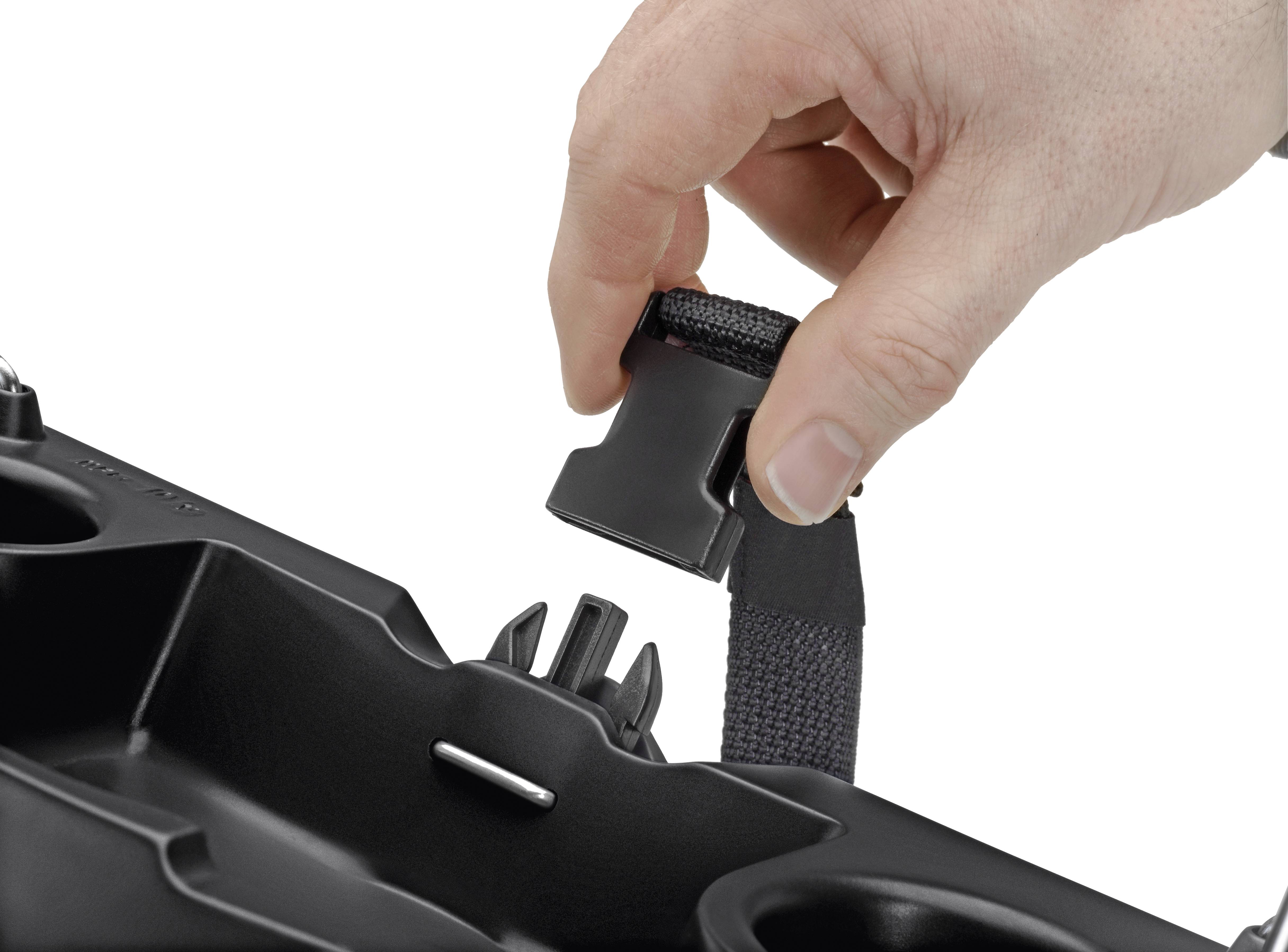 A hand holds a seat belt clip over a black car seat insert with drink holders and mounting points.