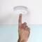 A hand presses the test button on a smoke detector on the ceiling.