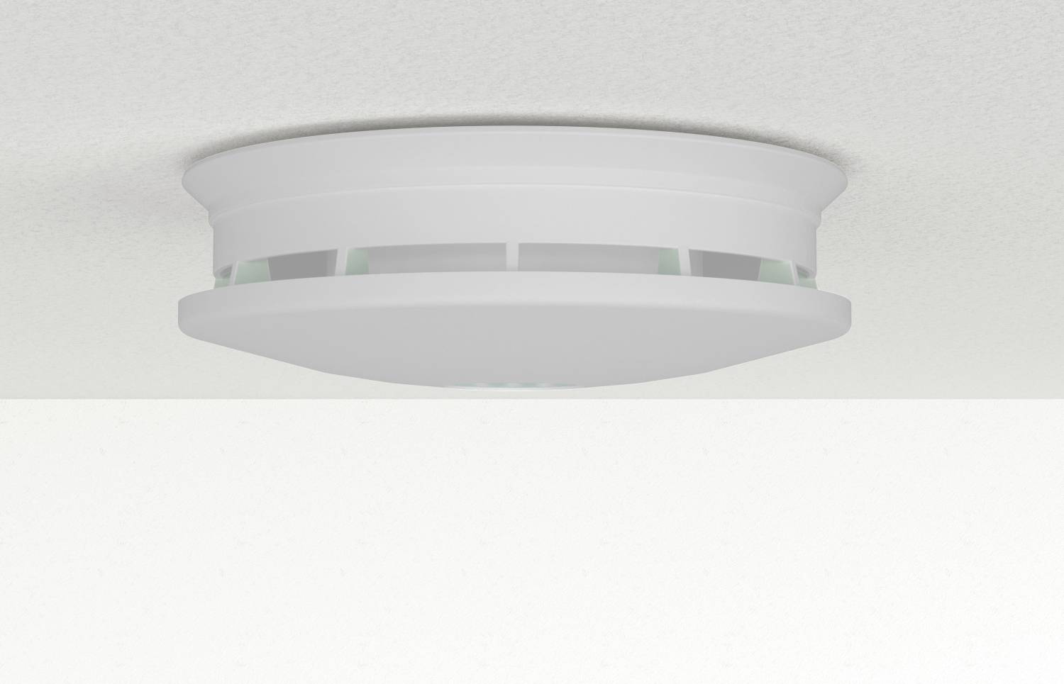 Ceiling-mounted smoke detector with a circular design, featuring slotted sides for air flow, set against a light-colored ceiling surface.