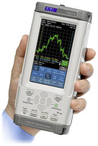 A hand is holding a portable RF spectrum analyser, displaying a frequency spectrum on a screen.